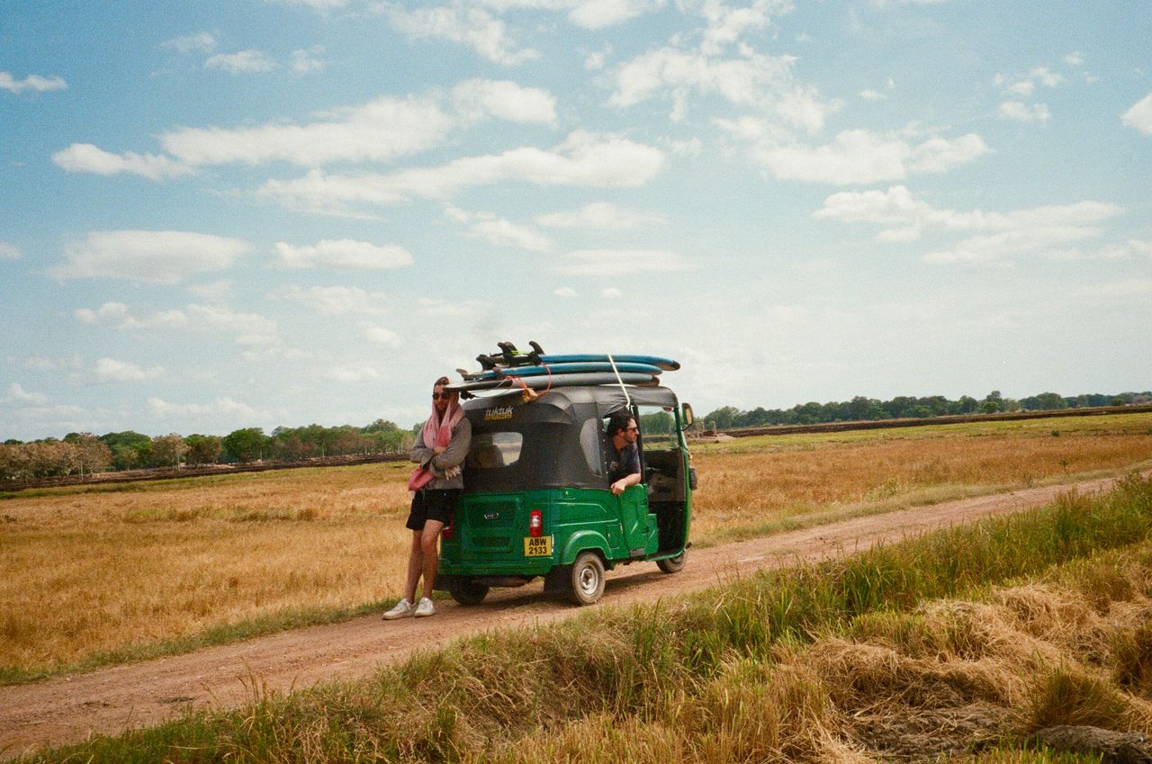 Two travelers with surfboards on a tuk-tuk explore the scenic landscapes of rural Sri Lanka.